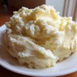 A generous serving of creamy, fluffy garlic mashed potatoes piled high on a white plate.