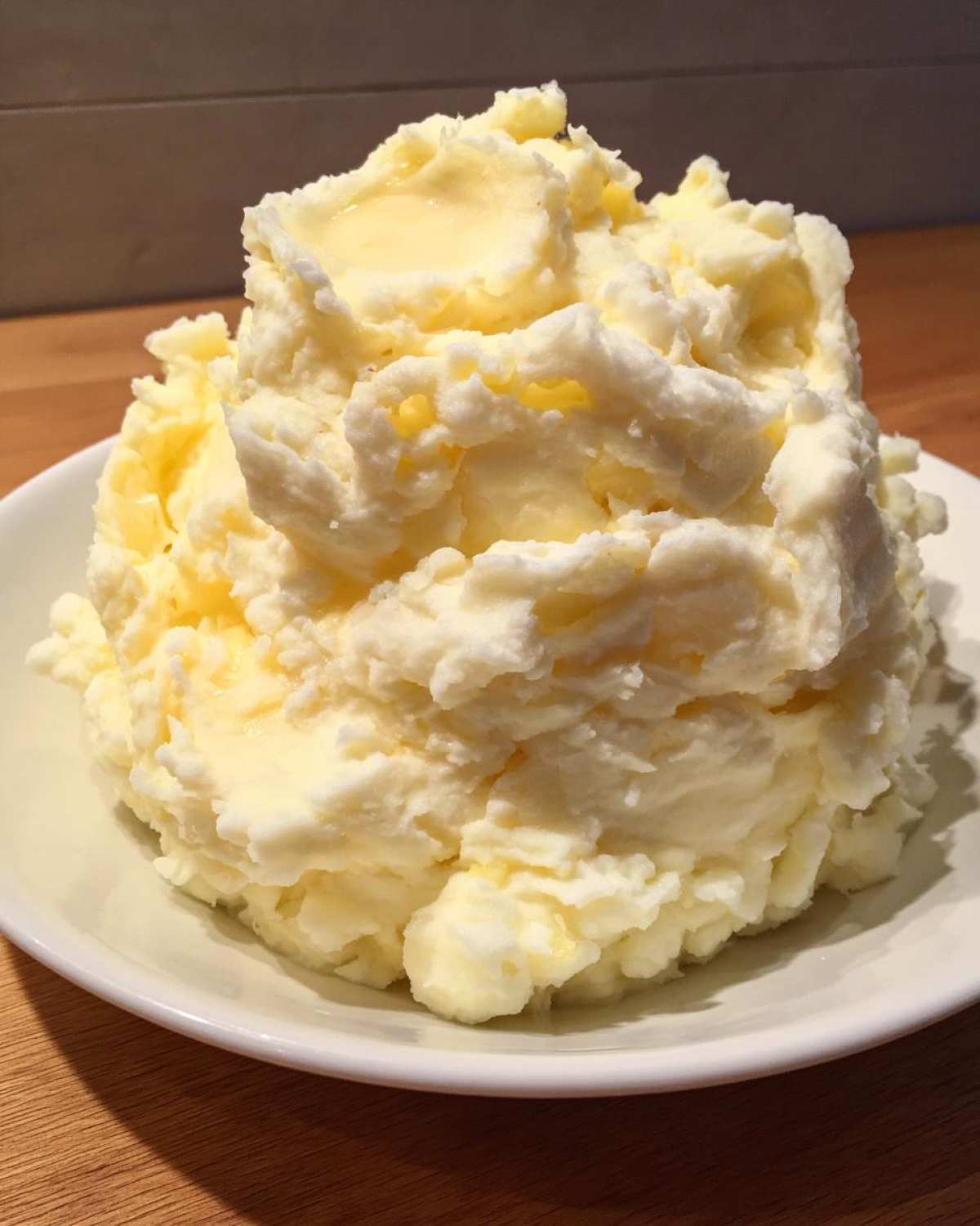 A large mound of fluffy, creamy garlic mashed potatoes topped with melting butter in a white bowl.