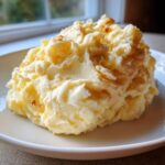 A generous serving of creamy, fluffy garlic mashed potatoes with visible flecks of browned butter or garlic, served on a white plate.