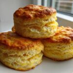 Three tall, flaky, golden brown scones stacked on a white plate, showing excellent rise.
