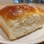 Close-up of a slice of incredibly soft japanese milk bread showing its fluffy interior and shiny, golden-brown crust.