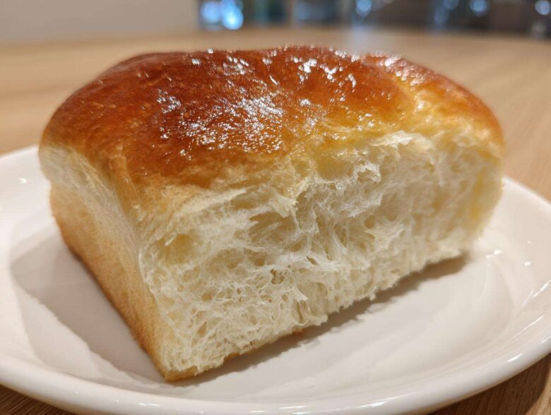 Close-up of a slice of incredibly soft japanese milk bread showing its fluffy interior and shiny, golden-brown crust.