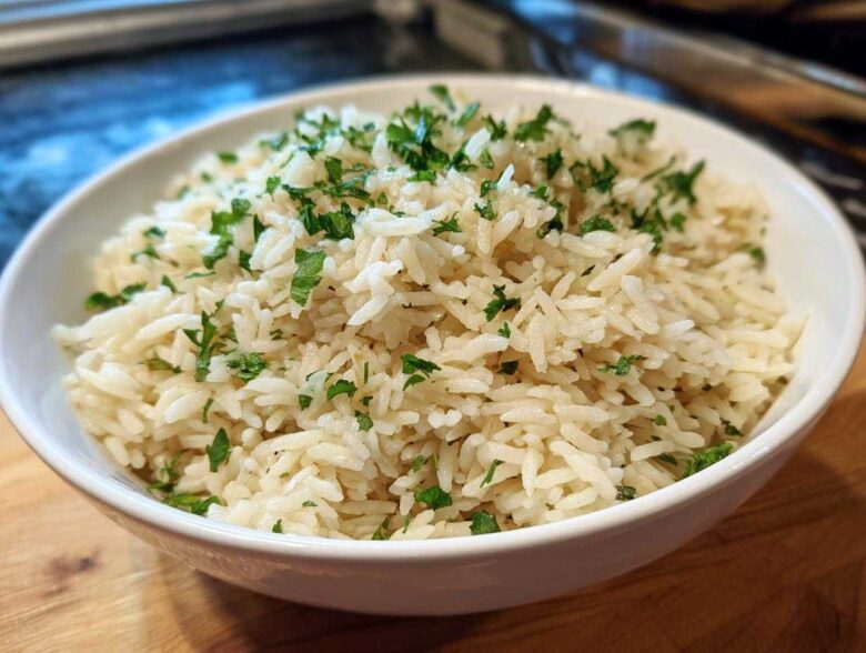 A close-up of fluffy white rice pilaf served in a white bowl and garnished with fresh chopped parsley.