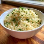Close-up of a white bowl filled with fluffy, perfectly cooked rice pilaf, garnished generously with fresh chopped parsley.