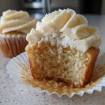 Close-up of a fluffy vanilla cupcake with a bite taken out, showing the moist crumb and vanilla frosting.
