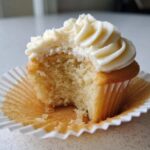 Close-up of a fluffy vanilla cupcakes with white frosting, showing a bite taken out to reveal the moist interior.