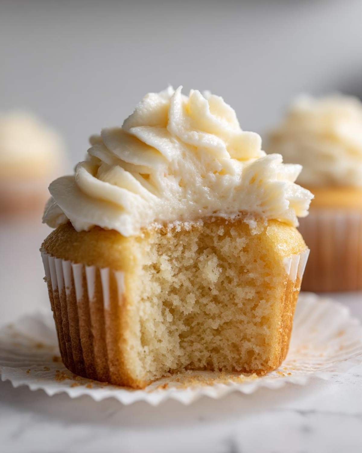 Close-up of a vanilla cupcake with a bite taken out, showing the fluffy crumb and white vanilla frosting.