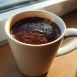 Close-up of rich, dark french hot chocolate steaming in a white mug, set near a window.