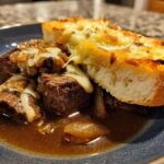Close-up of tender beef chunks in rich broth, topped with caramelized onions and melted cheese, served with cheesy toasted bread, a perfect french onion beef stew.