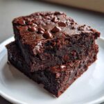 Two fudgy black bean brownies stacked on a white plate, topped with melted chocolate chips.