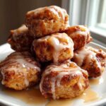 A stack of golden brown apple fritter bites drizzled generously with a light glaze, served on a white plate.