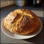 A freshly baked, round loaf of golden brown soda bread resting on a white plate.