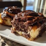 Two gooey chocolate cinnamon rolls heavily frosted with rich chocolate glaze, sitting on a white plate.