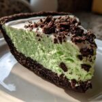 A close-up slice of creamy, light green grasshopper pie with a dark chocolate crust and chocolate crumbles on top.