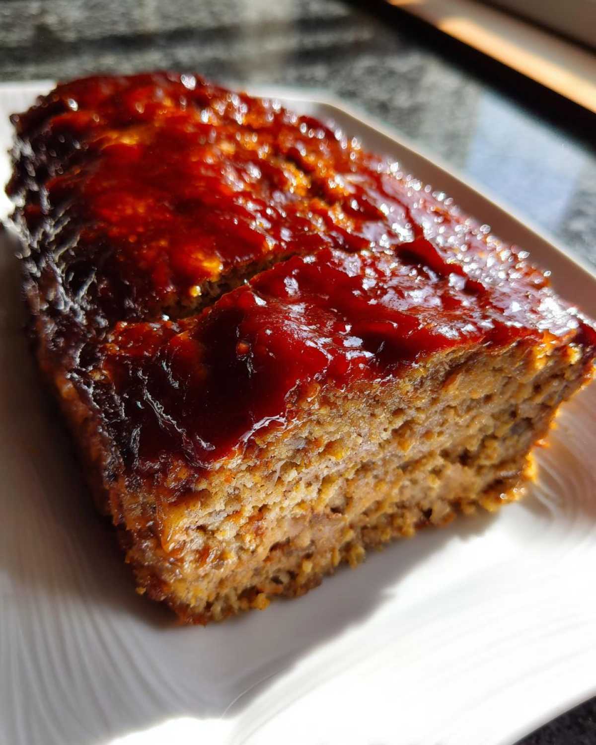 A close-up of a thick slice of juicy meatloaf topped with a thick, glossy, dark red glaze.