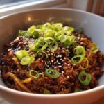 Close-up of a savory keto egg roll in a bowl with ground meat, sauce, topped with sesame seeds and fresh green onions.