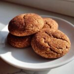 Four soft, crackled snickerdoodle cookies heavily coated in cinnamon sugar, stacked on a white plate.