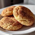 Three soft, thick snickerdoodle cookies generously coated in cinnamon sugar, resting on a white plate.