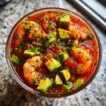 Overhead view of vibrant Mexican shrimp cocktail filled with plump shrimp, diced avocado, and cilantro in a rich tomato-based sauce.