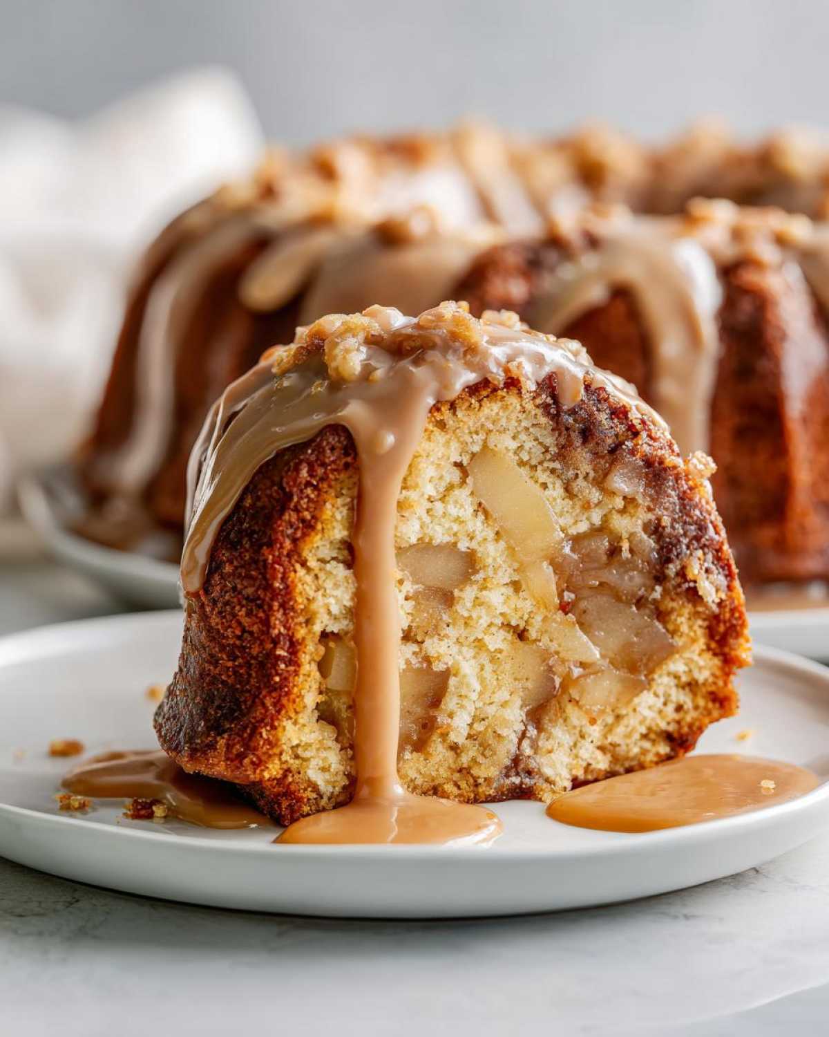 A close-up slice of moist apple bundt cake filled with cooked apples, topped with caramel glaze and nuts.