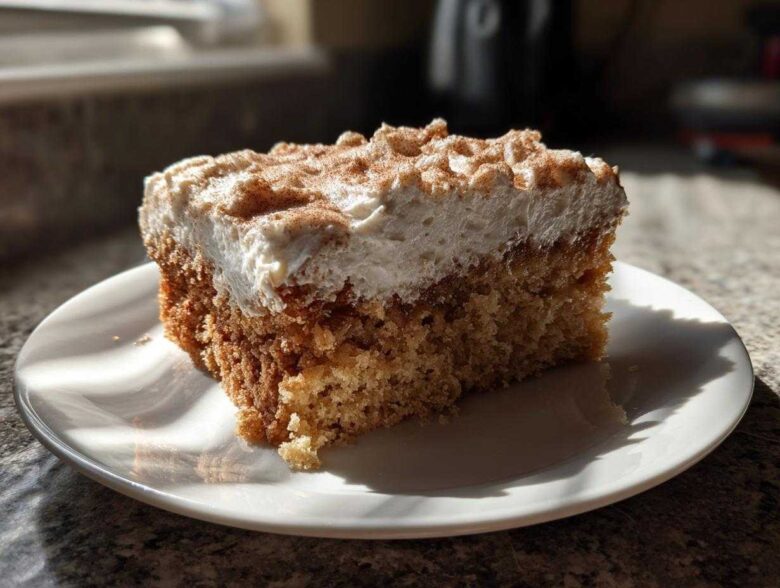 A square slice of moist applesauce cake topped with thick white frosting and dusted with cinnamon.