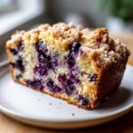 Close-up of a moist slice of blueberry banana bread featuring visible blueberries and a crumbly streusel topping.