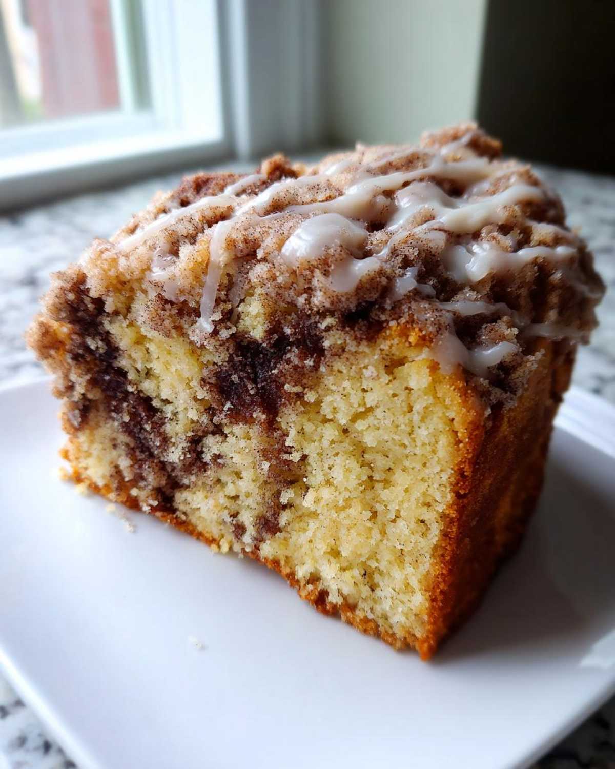 Close-up of a moist slice of coffee cake featuring a cinnamon swirl and sweet vanilla glaze topping.