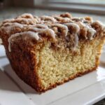 Close-up of a moist slice of coffee cake featuring a thick cinnamon streusel topping and white vanilla glaze.