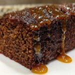 Close-up of a rich, dark slice of gingerbread cake topped with a thick, dripping amber glaze.