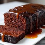 Close-up of a slice of moist gingerbread cake drizzled generously with a thick, glossy caramel or toffee sauce.
