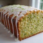 A close-up view of a freshly baked loaf of lemon zucchini bread topped with white glaze and zest.