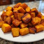 A pile of perfectly caramelized and seasoned roasted sweet potatoes cubes served on a white plate.