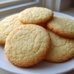 A stack of five golden-brown, round sugar cookies with a slightly crackled top, resting on a white plate.