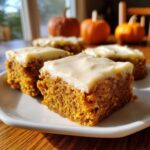 Close-up of moist pumpkin bars topped with thick cream cheese frosting, served on a white plate.