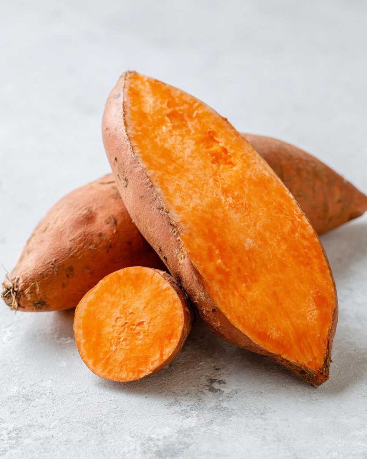 Close-up of raw sweet potatoes, one halved lengthwise showing bright orange flesh, ready for baking.
