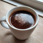 Close-up of rich, dark french hot chocolate with small bubbles on the surface in a white mug.
