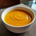 Close-up of a vibrant orange bowl of roasted butternut squash soup, garnished with cracked black pepper.