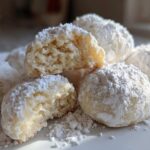 A close-up of several Russian tea cakes heavily dusted with powdered sugar, one is broken open showing the crumb.