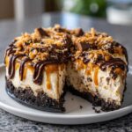 A slice removed from a rich Samoa Cheesecake showing the thick crust, creamy filling, and toppings of caramel, chocolate, and toasted coconut.