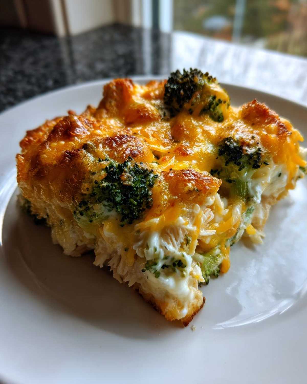 A close-up of a square serving of baked Chicken Divan casserole with melted cheddar cheese and broccoli florets.