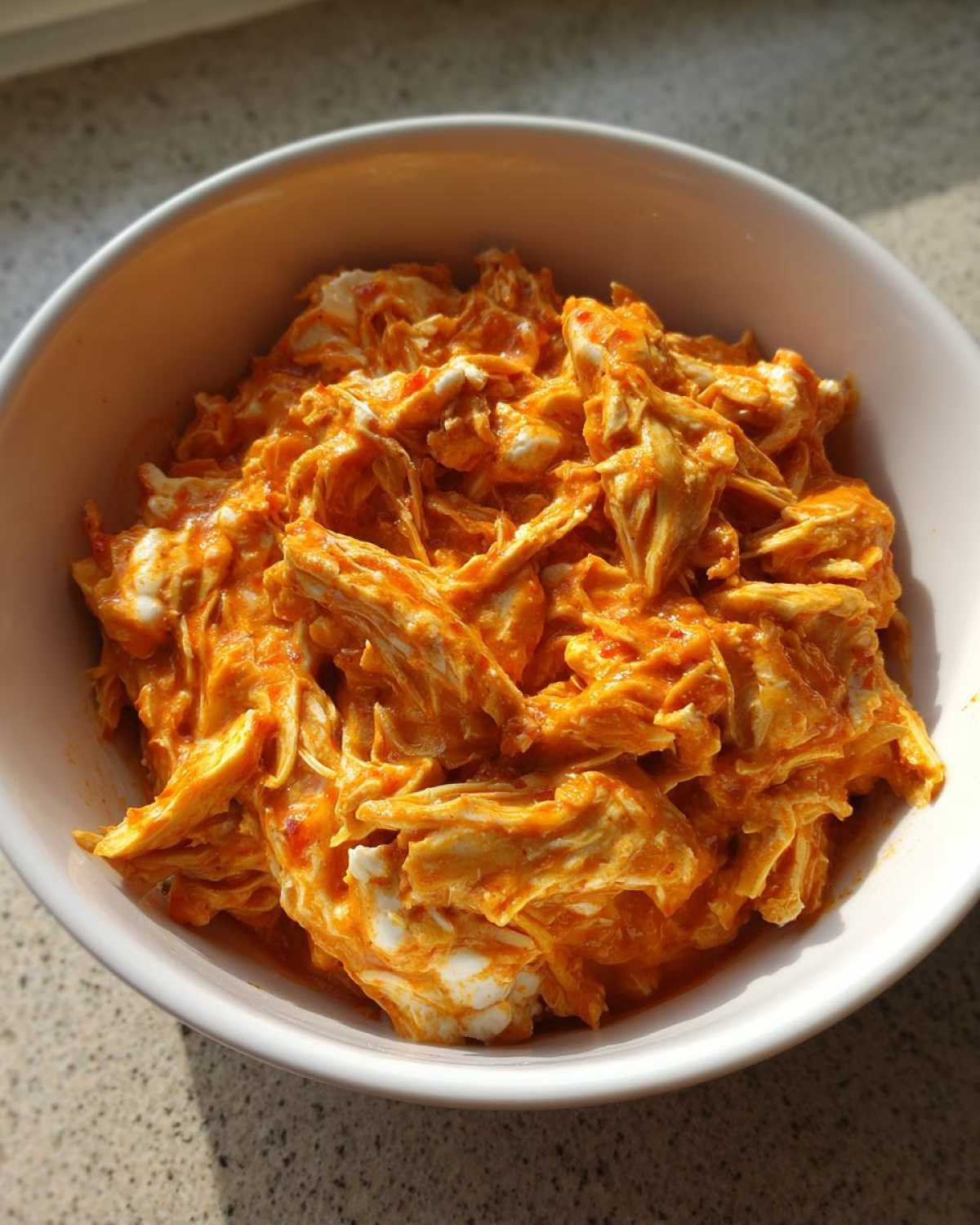 Close-up of shredded chicken coated in creamy orange buffalo sauce, ready for slow cooker buffalo chicken chili.