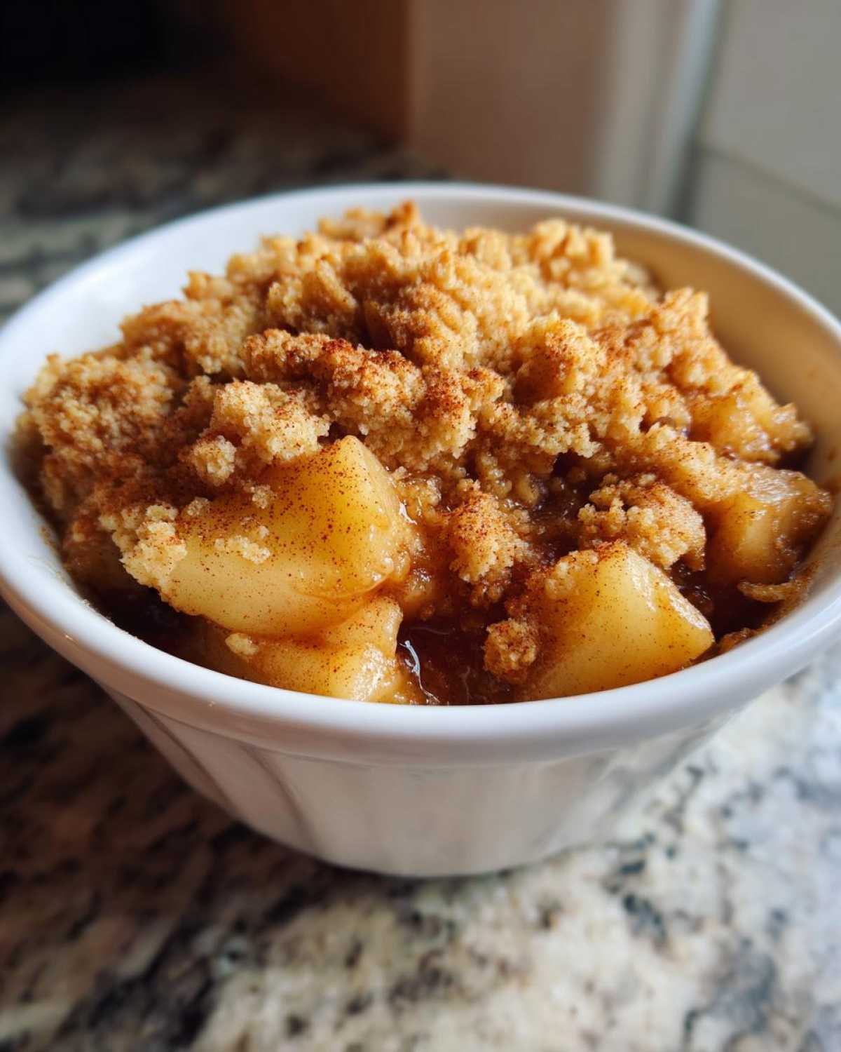 Close-up of a warm, single-serving apple crumble with a buttery topping and cinnamon dusting.