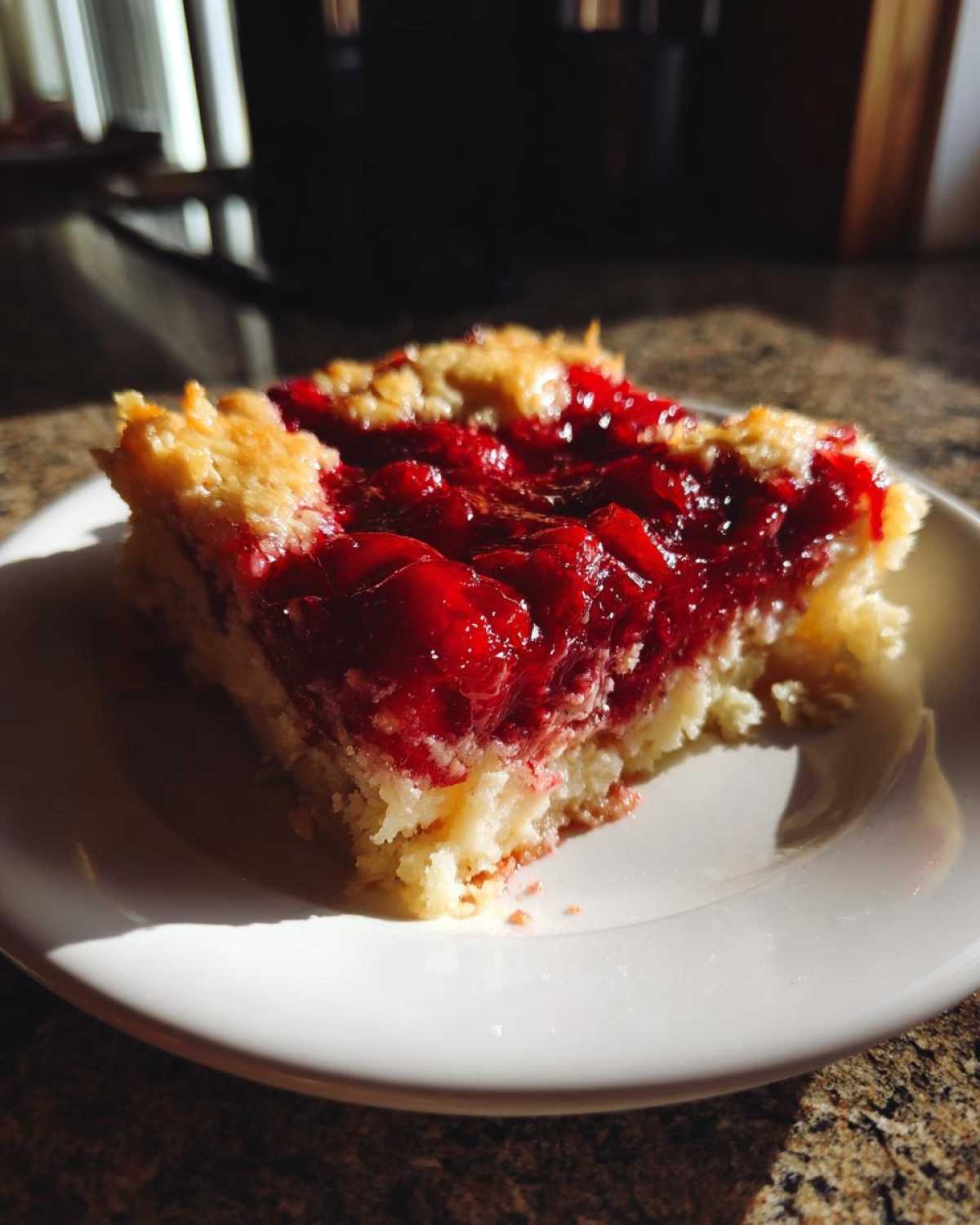 A close-up, sunlit slice of cherry dump cake showing the bright red cherry filling over a light cake base.