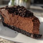 A thick slice of creamy chocolate cheesecake with a dark chocolate crust and crumbled topping.
