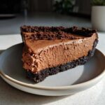 A thick slice of no-bake chocolate cheesecake with a dark crust and chocolate crumbs on top.