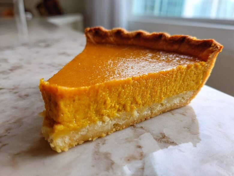 A close-up side view of a perfect slice of easy pumpkin pie showing the bright orange filling and golden crust.