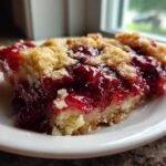 Close-up of a moist slice of cherry dump cake with a crumbly topping served on a white plate.