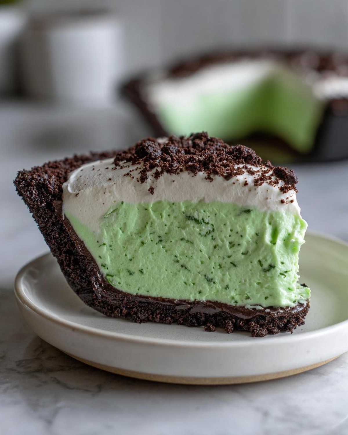 A close-up slice of grasshopper pie featuring a dark chocolate crust, bright green mint filling, and whipped topping.