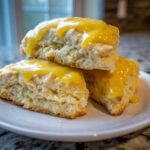 Three soft lemon scones stacked on a white plate, generously topped with a bright yellow lemon glaze.