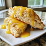 Two halves of soft lemon scones stacked and generously covered in a bright yellow lemon glaze.